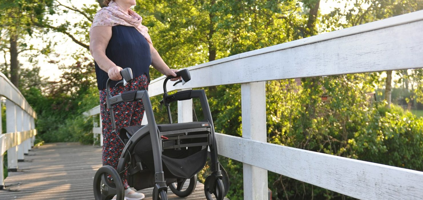 A lady standing on a bridge with her walking frame enjoying the outdoors with confidence.