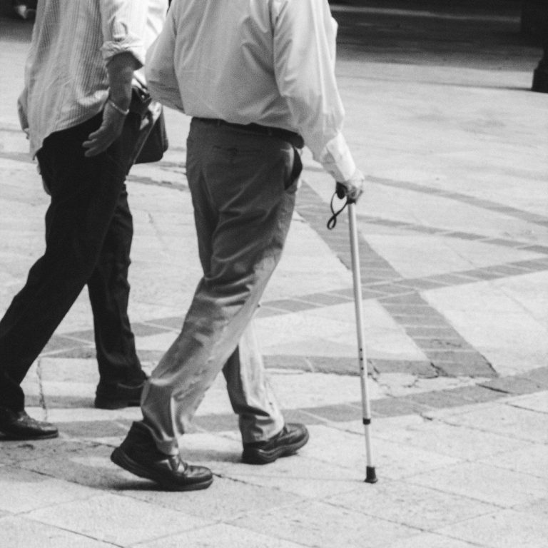 Two people walking, one using a walking stick to emphasise gait reeducation and mobility rehabilitation.